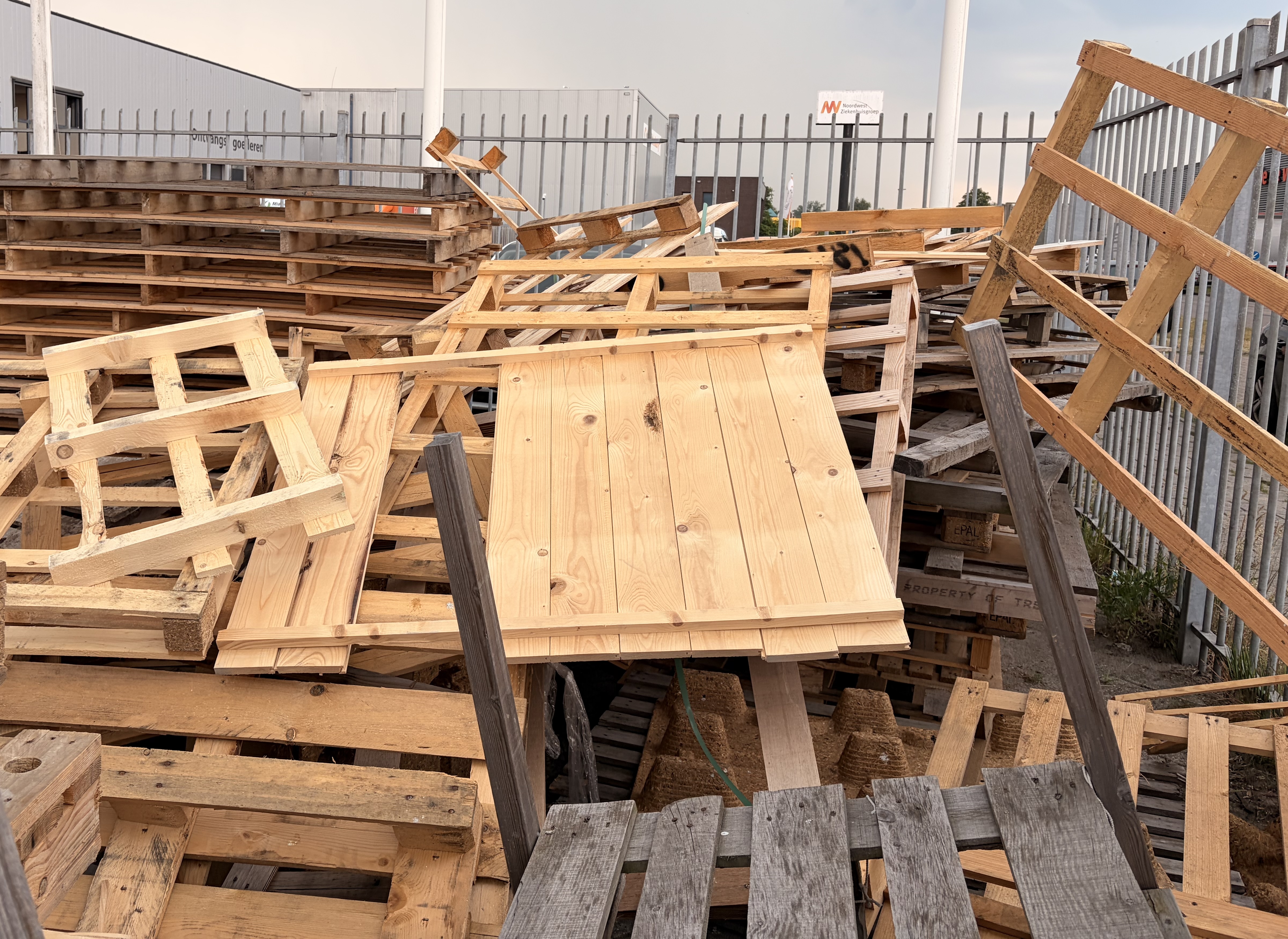 Stapel oude houten pallets achter een hek